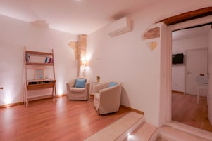 Un soggiorno con pavimento in legno, una libreria, due poltrone, un tavolino con una lampada e una televisione sullo sfondo.