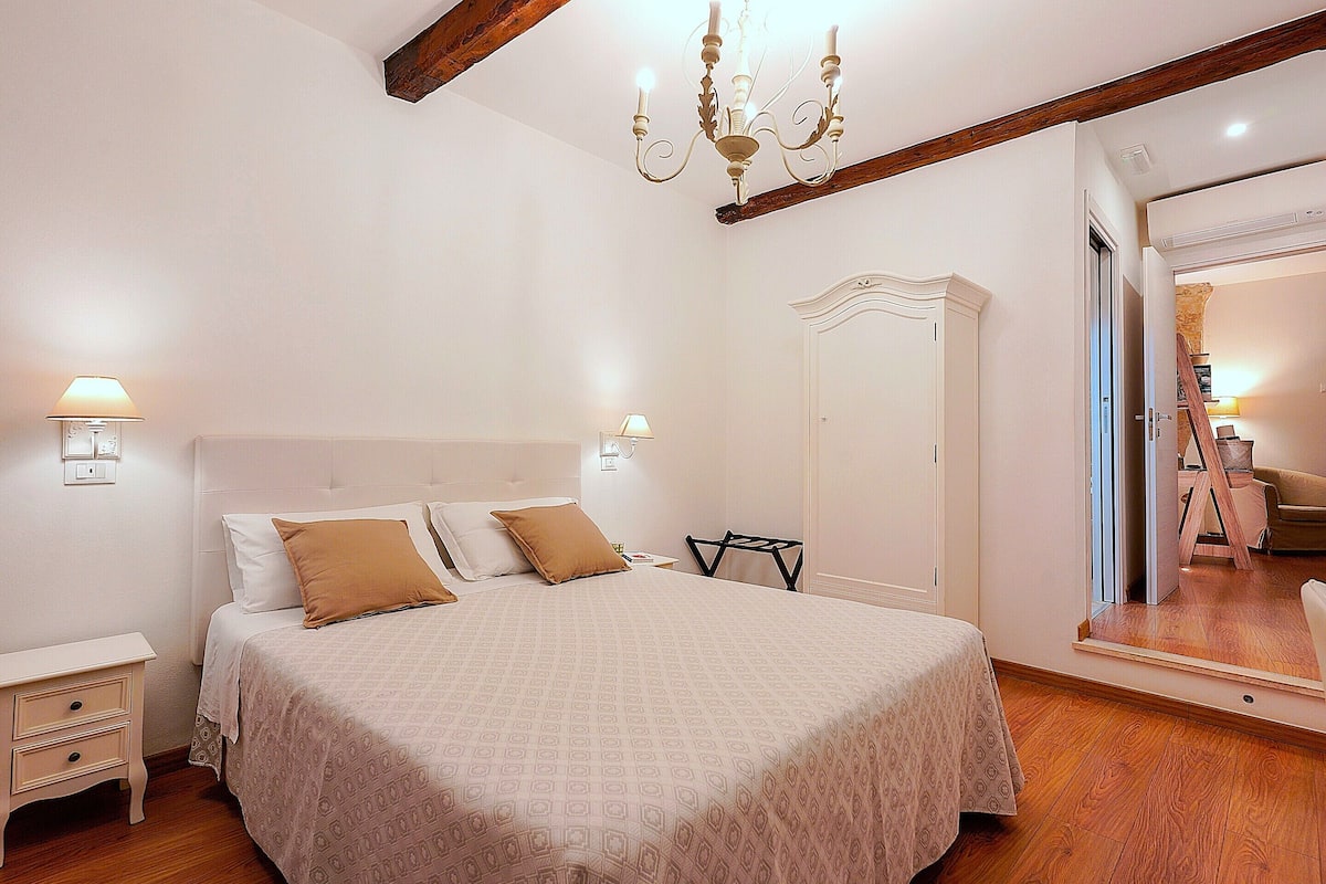 Une chambre à coucher comprenant un lit, des tables de chevet, une armoire, un miroir et un lustre.