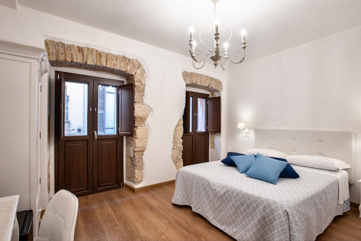 Une chambre avec un grand lit, des murs en pierre, des portes en bois et un lustre.