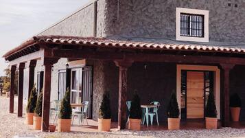 Un bâtiment doté d’une façade en pierre, d’un toit en tuiles et d’un patio couvert avec des sièges d’extérieur.
