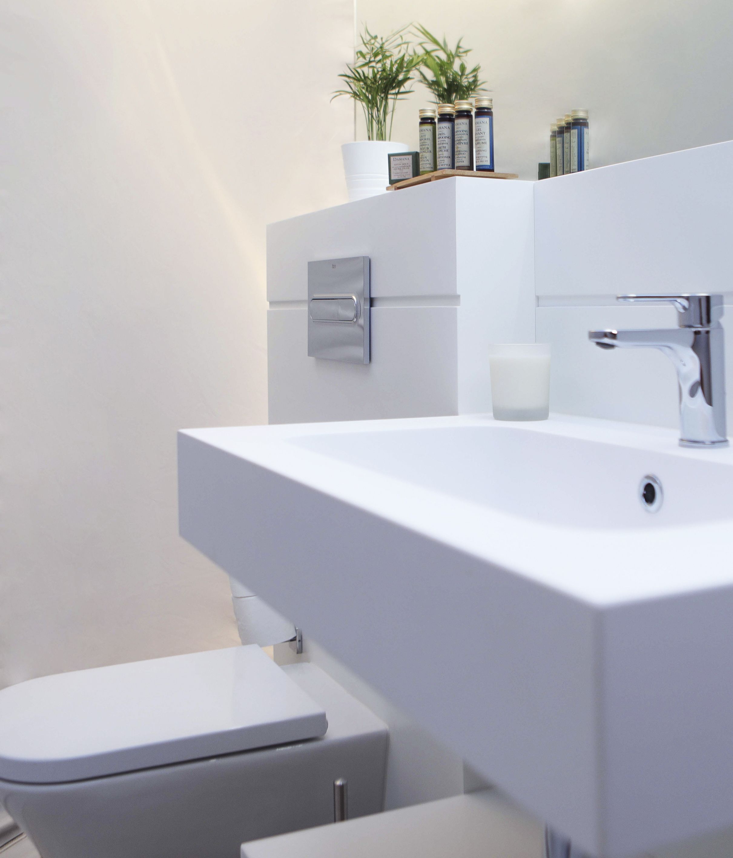 Un baño moderno con un lavamanos blanco, un inodoro y un mueble con artículos de aseo.