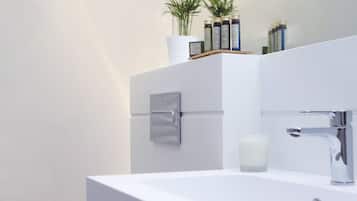 Un baño moderno con un lavamanos blanco, un inodoro y un mueble con artículos de aseo.