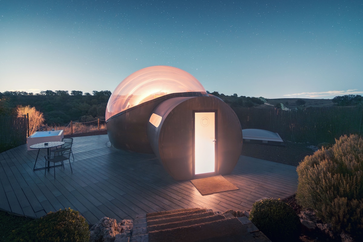 A spherical structure with an open door, a wooden deck, and a small table with chairs.