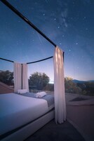 Un dormitorio con cama, cortinas blancas y vistas al cielo nocturno.