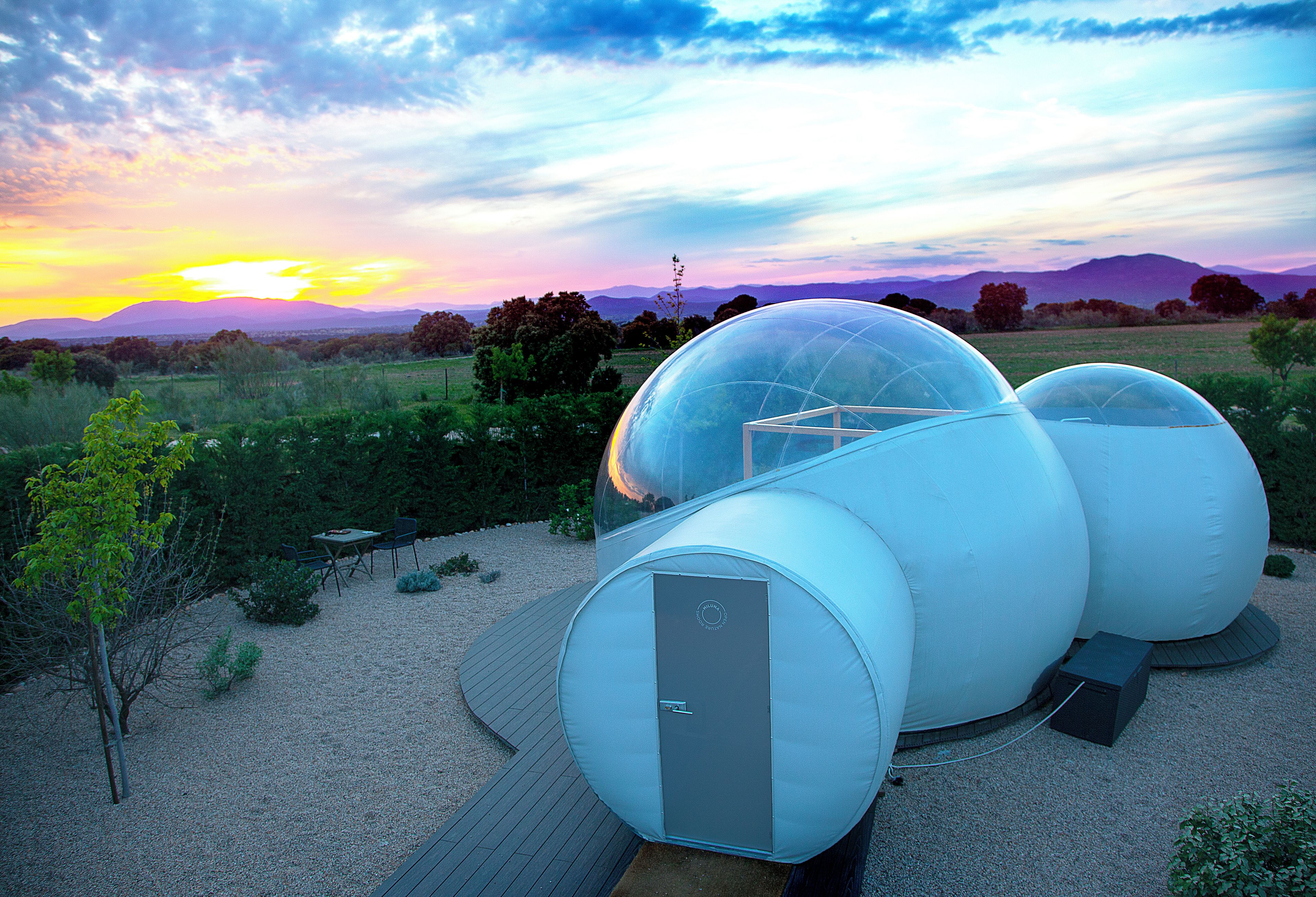 Una estructura esférica moderna con una cúpula transparente, rodeada por una zona de grava y una terraza de madera.
