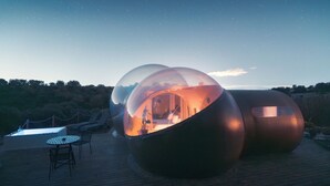 Two transparent spherical structures with interior lighting, a wooden deck, and lounge chairs. - Miluna (Hormigos)