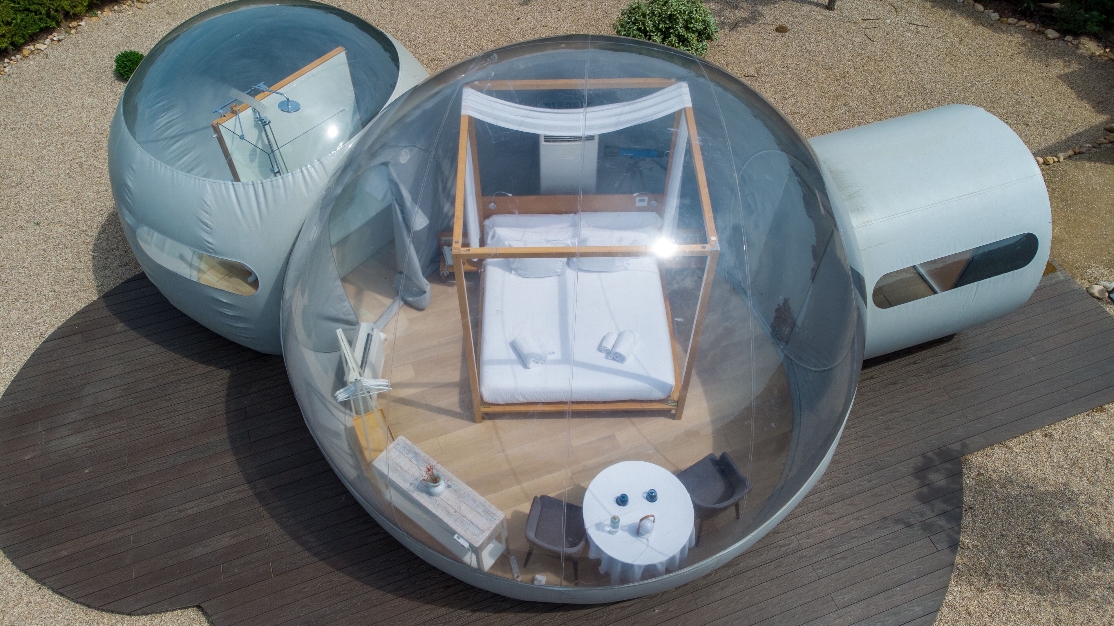 A transparent spherical room with a bed, a small table, and a chair.
