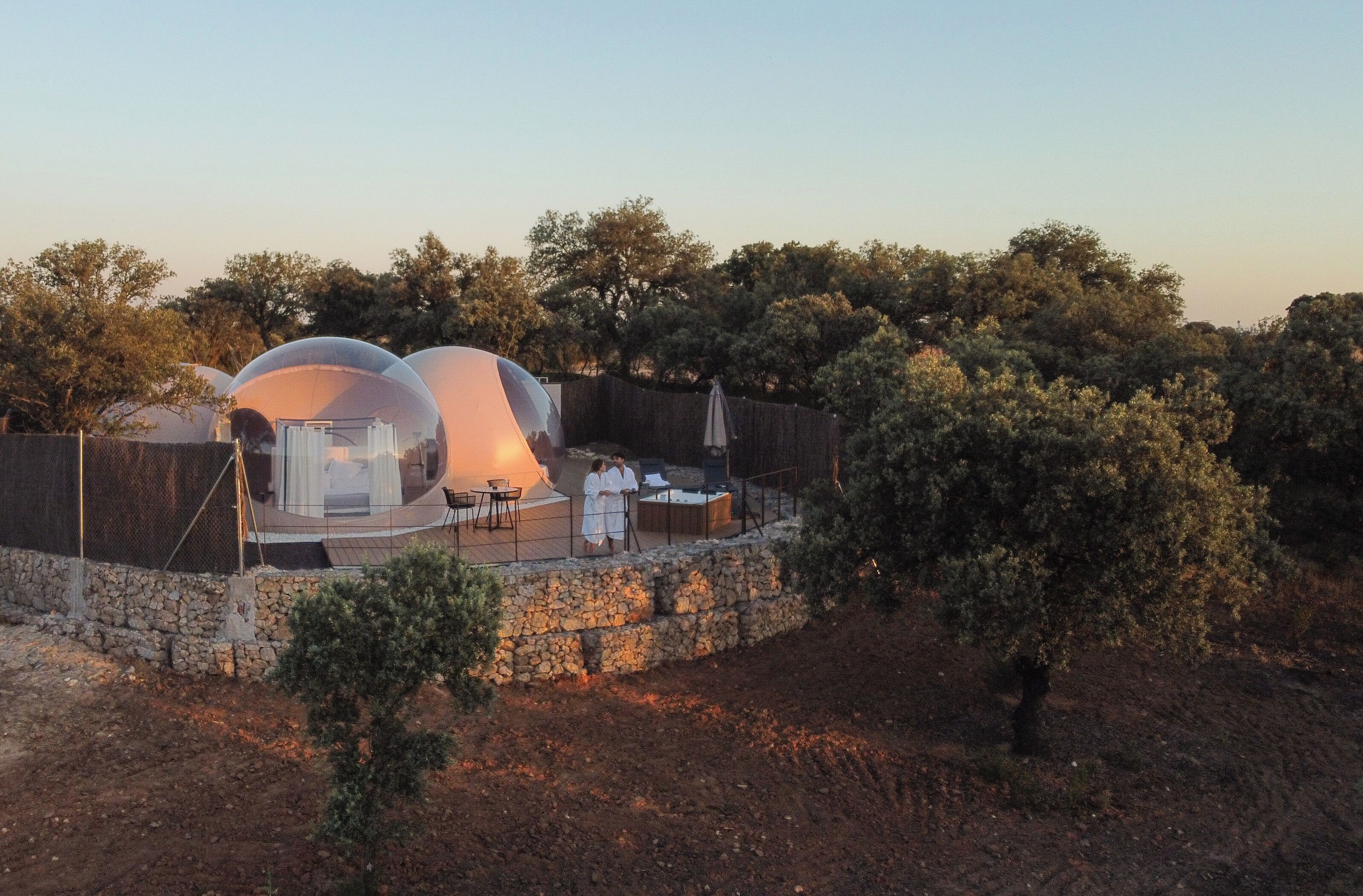 A transparent dome structure with outdoor seating and a stone wall.