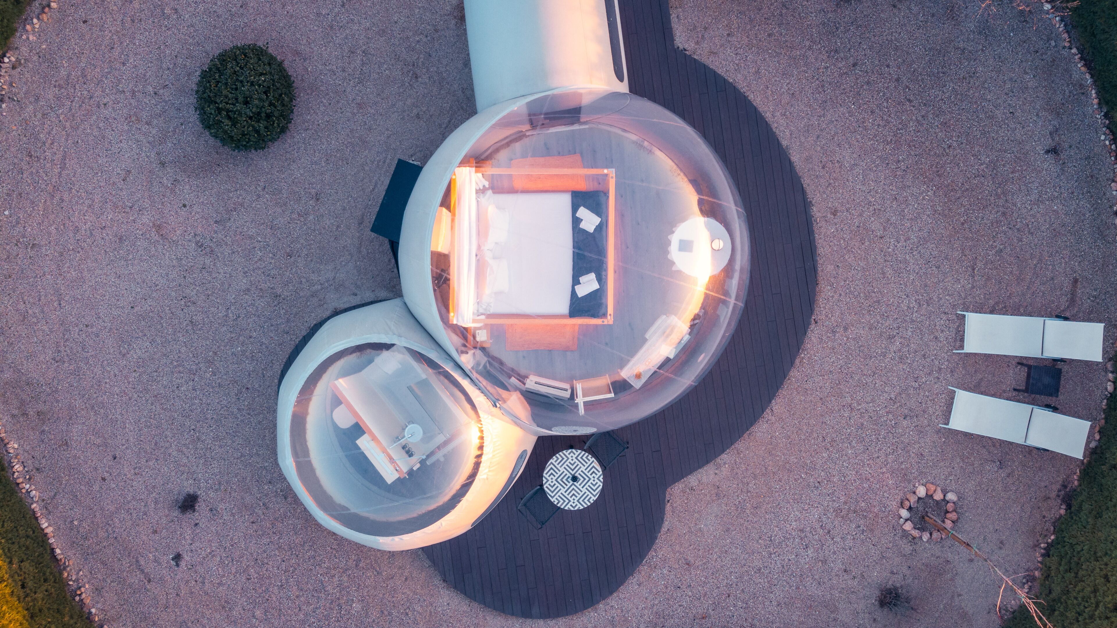 Une vue aérienne d’un bâtiment circulaire doté d’une cour intérieure, de deux structures circulaires plus petites et d’une zone pavée avec un petit arbre et un arrangement circulaire de pierres.