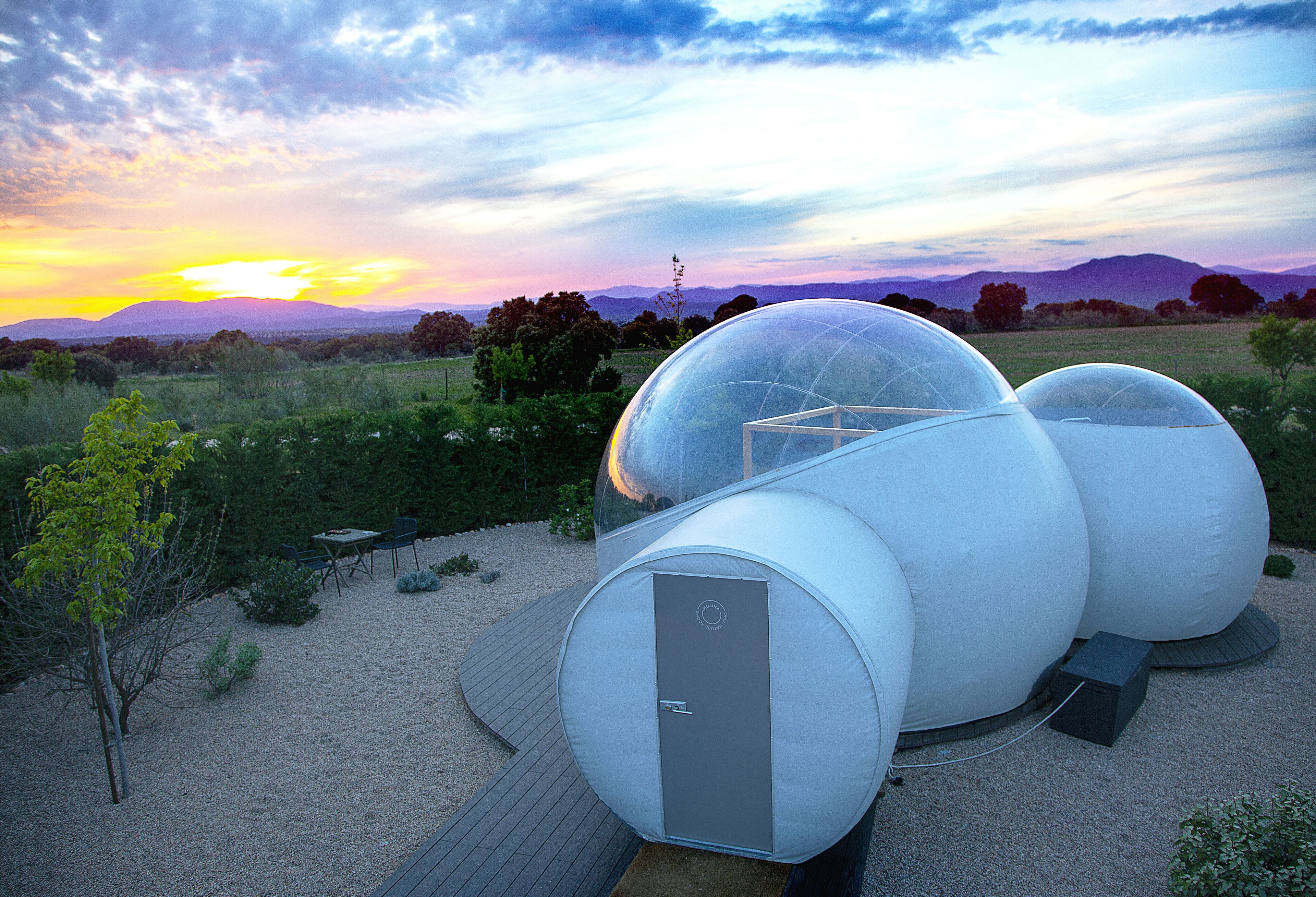 A modern spherical structure with a transparent dome, surrounded by a gravel area and a wooden deck.