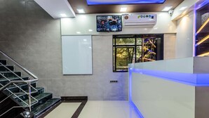 A modern lobby with a staircase, a reception desk, a large window with a view, and a mounted television. - Hotel Plaza Mumbai (Mumbai)