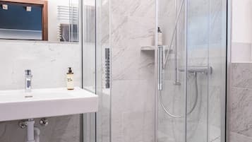 Un baño moderno con cabina de ducha de vidrio, un lavabo blanco y suelo de baldosas de mármol.