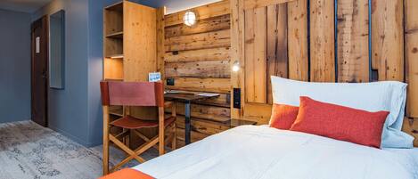 Un dormitorio con cabecera de madera, cama con ropa de cama blanca y roja, un escritorio con silla y un pequeño estante.