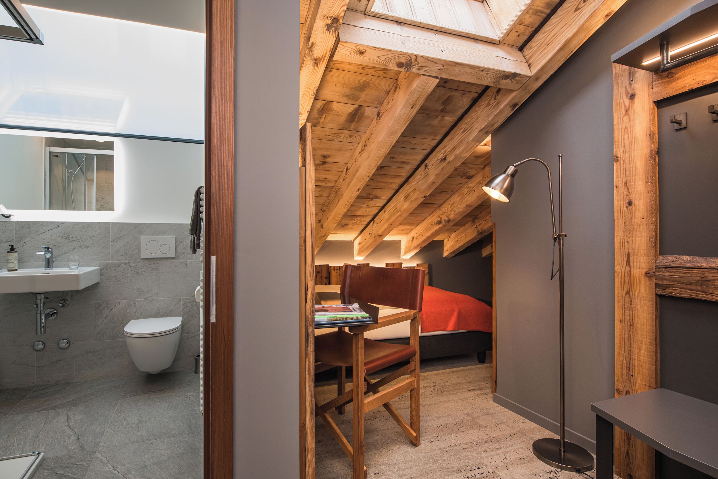 Un baño moderno y compacto con tragaluz, una silla de madera y una mesita de noche.