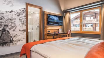 Habitación de hotel con cama, televisor montado en la pared, escritorio con silla y ventana con vistas a un edificio.