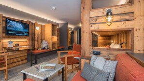 A cozy, rustic interior with wooden walls, a large flat-screen TV, seating areas, and a fireplace. - Hotel Basecamp (Zermatt)