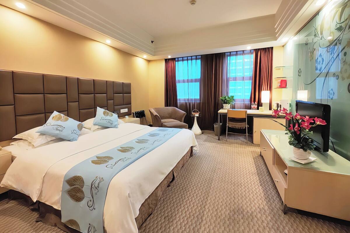 Een hotelkamer met een groot bed, een bureau, een stoel, een televisie en een raam met gordijnen.