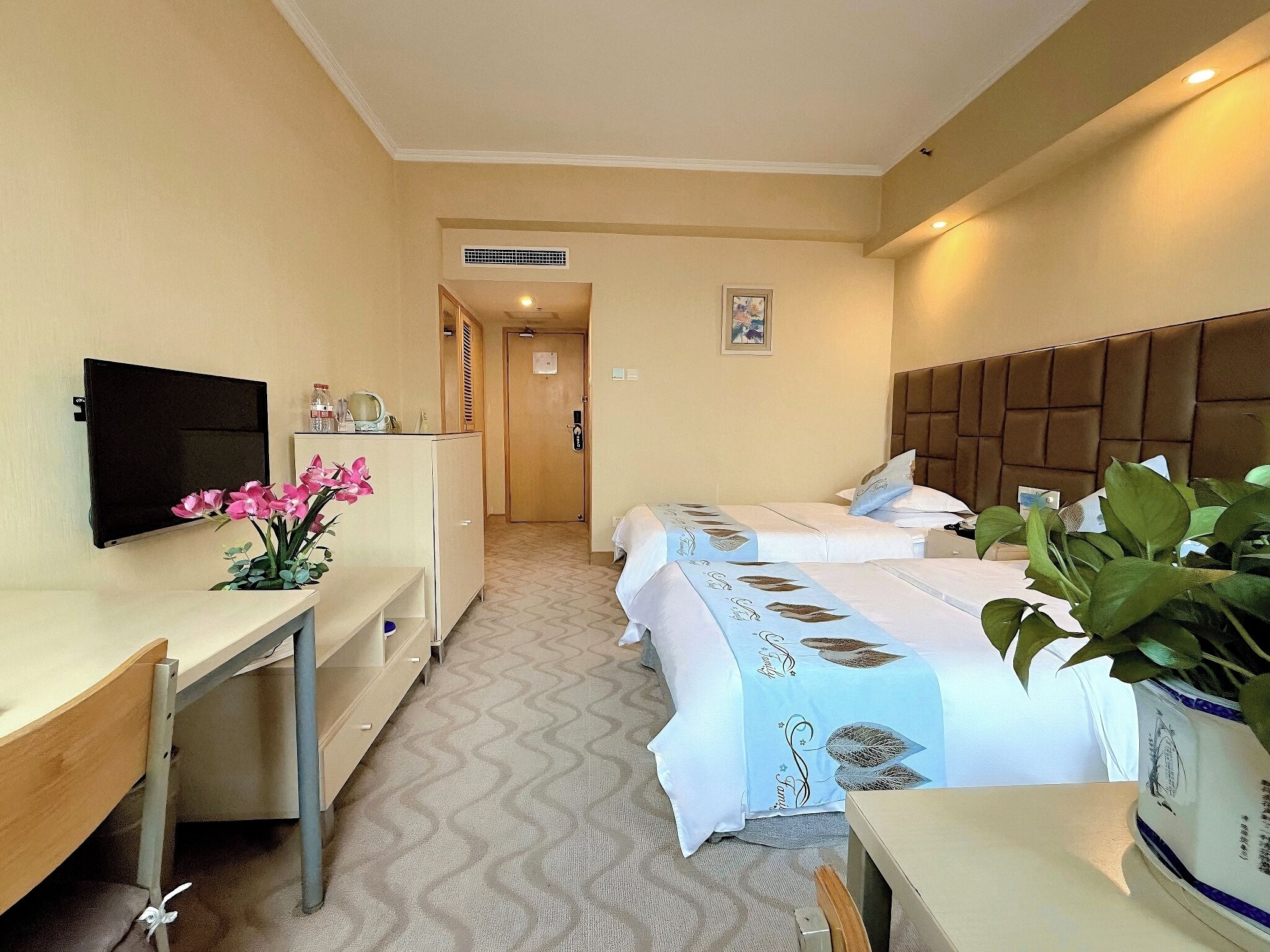 Habitación de hotel con dos camas, un escritorio, un televisor y una pequeña kitchenette.