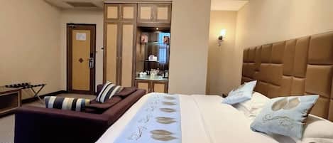 A hotel room with a large bed, a sofa, a desk, and a wardrobe.