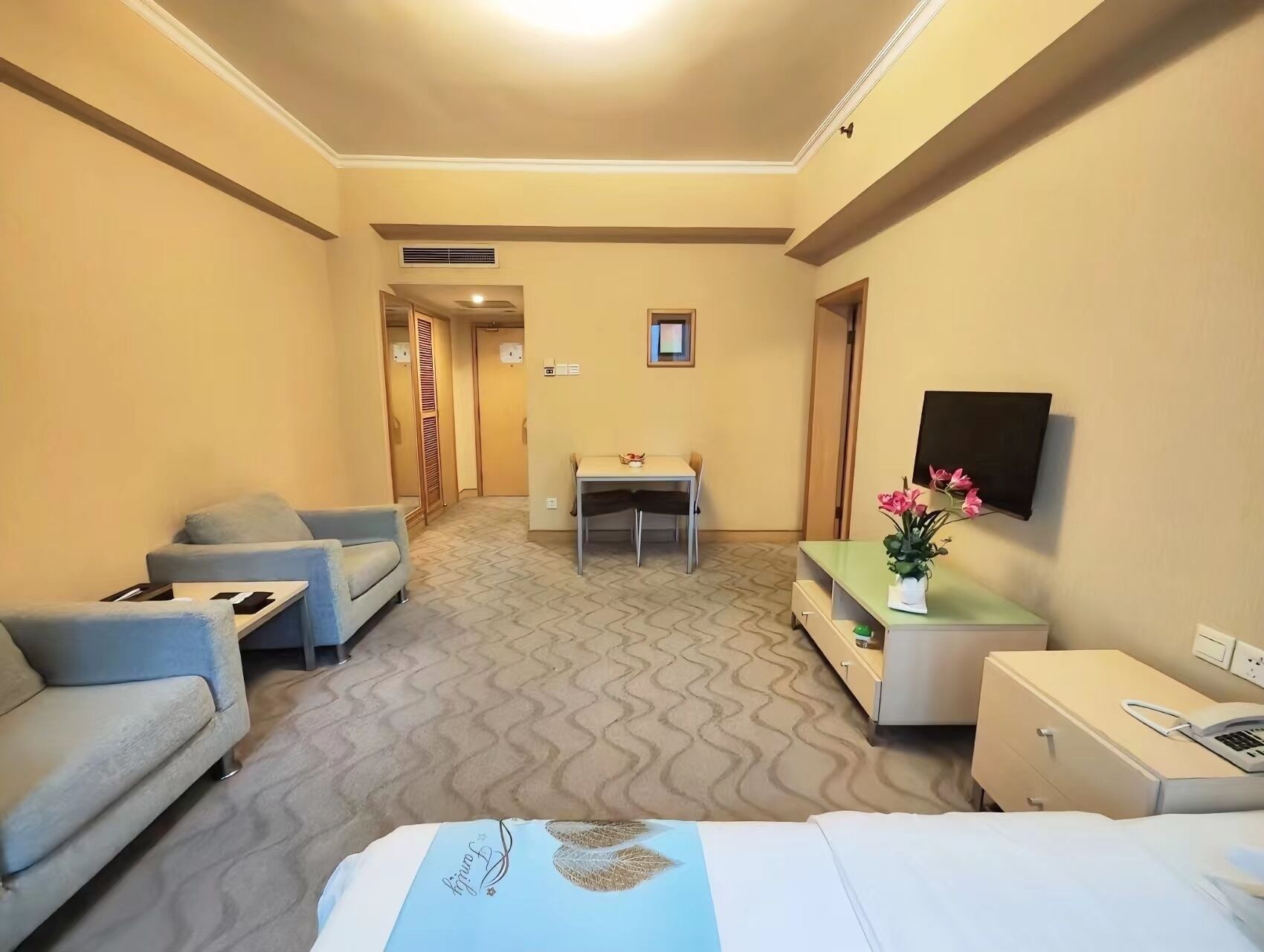 Habitación de hotel con cama, escritorio, silla, sofá, televisor y una pequeña mesa con un jarrón de flores.