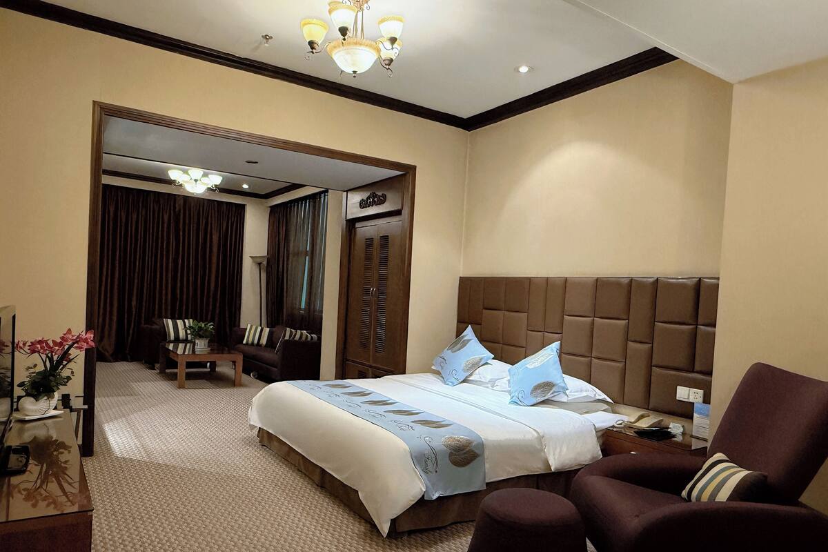 Een hotelkamer met een groot bed, een bruine fauteuil, een kleine tafel en een kledingkast.