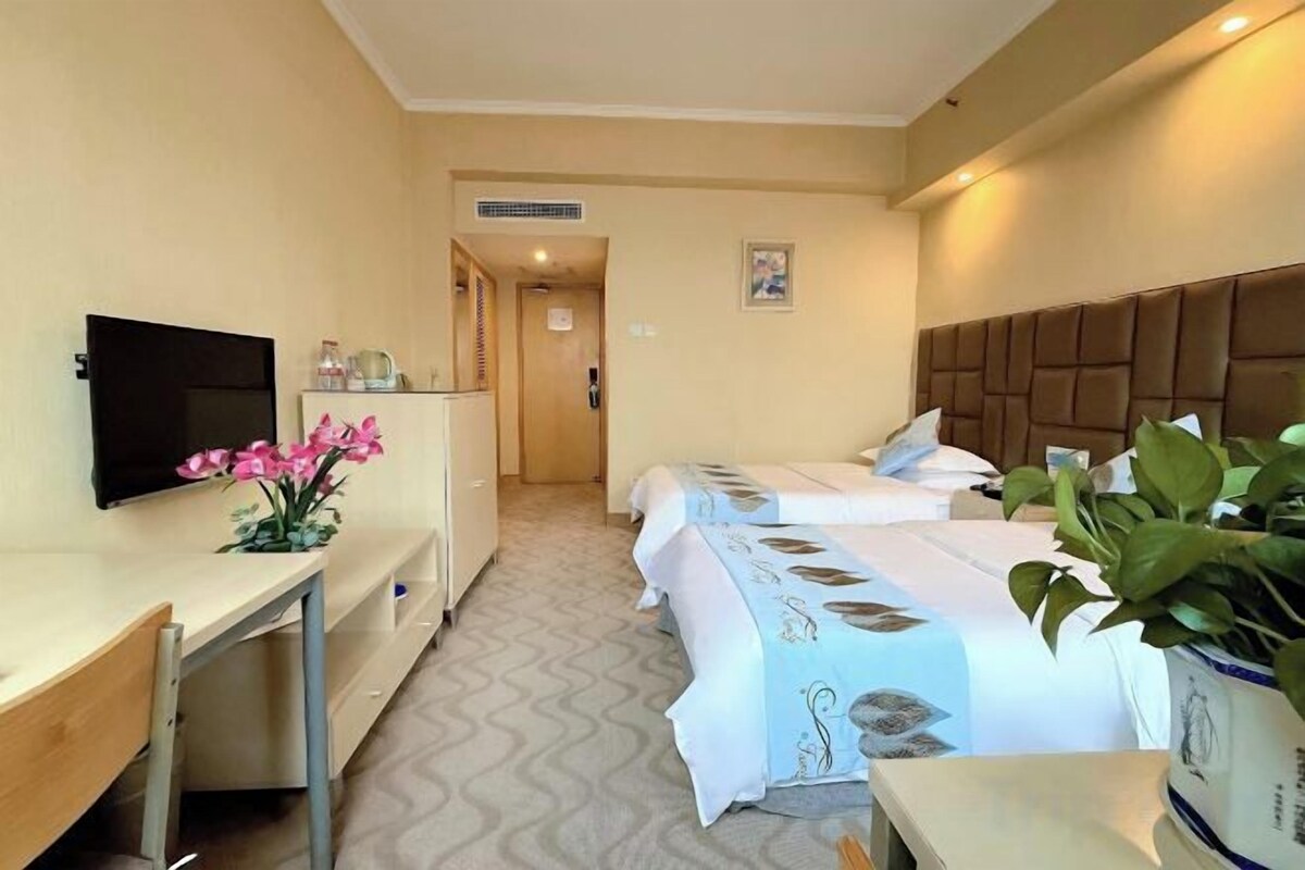 A hotel room with a bed, a desk, a television, and a potted plant.