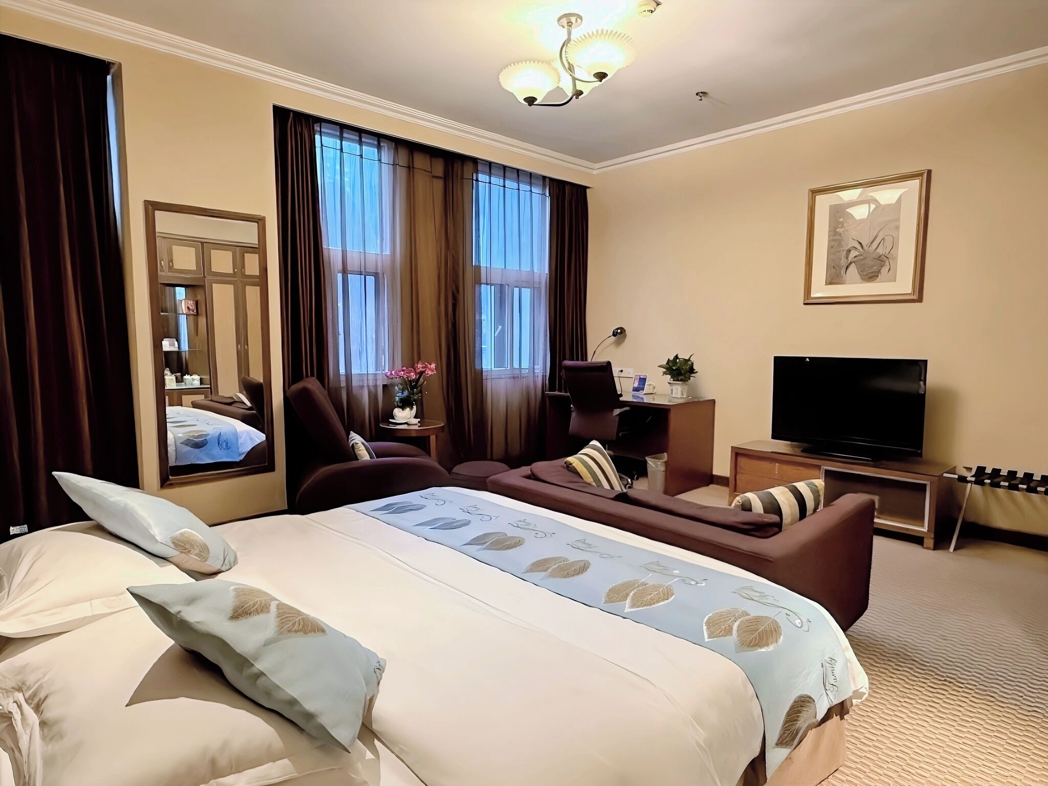 A hotel room with a large bed, a desk with a computer, a TV, and a seating area with a chair and a sofa.