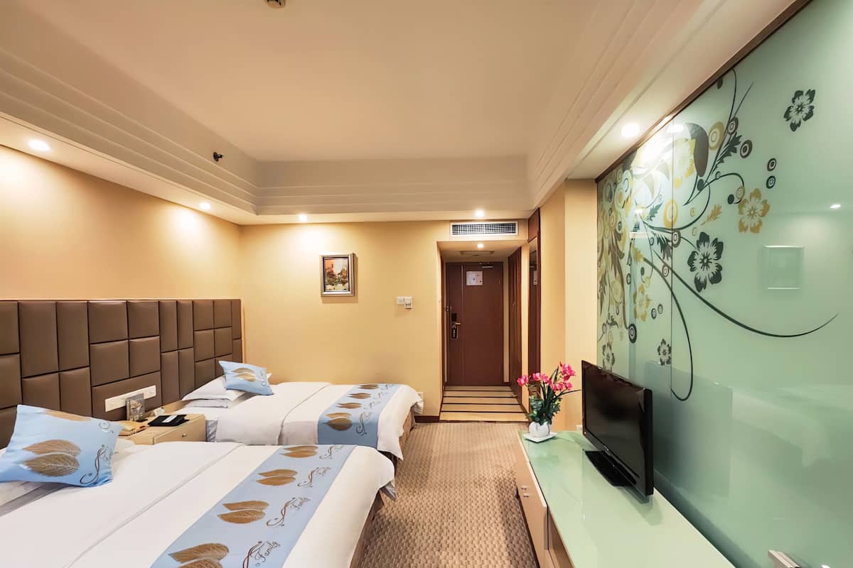 Een hotelkamer met twee bedden, een flatscreen televisie, een klein bureau en een decoratieve wand.