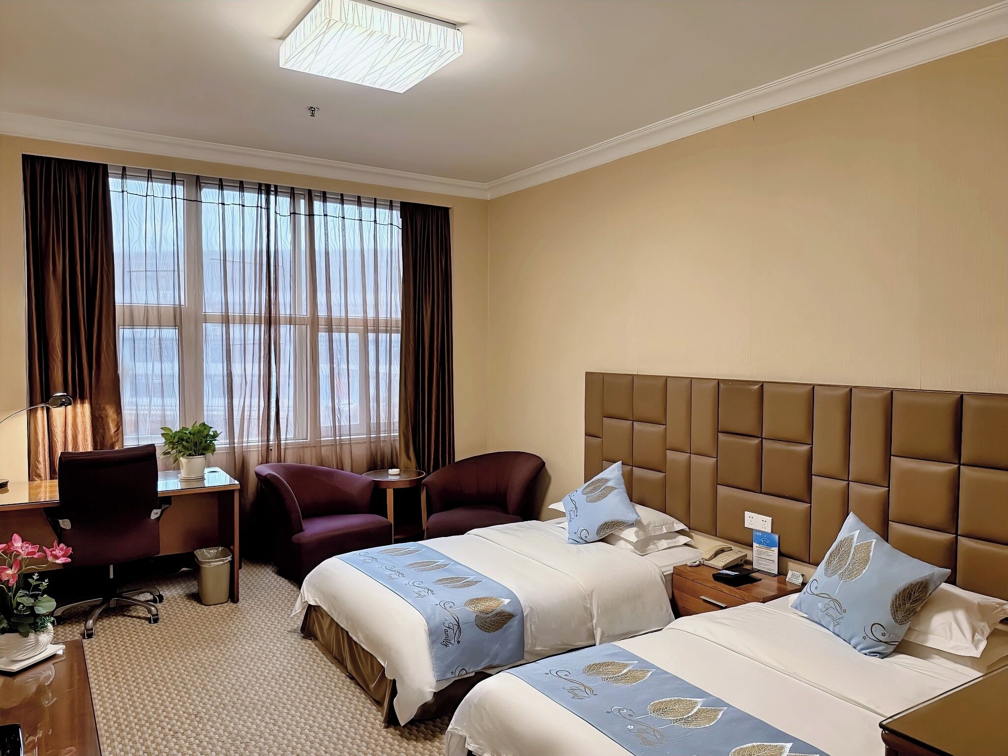 Ein Hotelzimmer mit zwei Betten, einem Schreibtisch, einem Stuhl, einer Lampe und einem Fenster mit Vorhängen.
