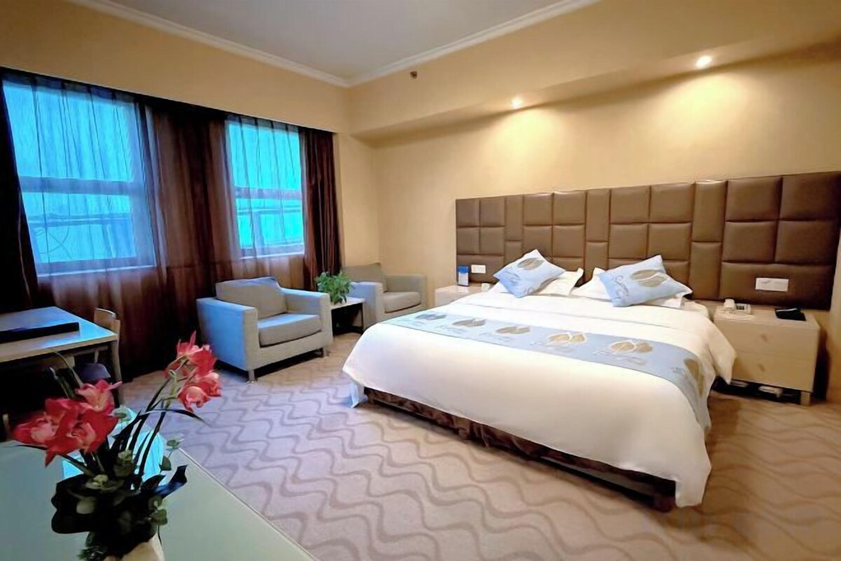 A hotel room with a large bed, a desk, a chair, and a window with curtains.