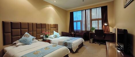 A hotel room with two beds, a desk, a chair, a TV, and a large window with curtains.
