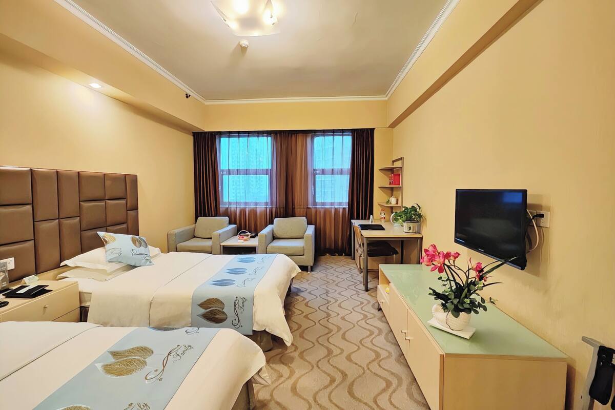 Hotelkamer met twee bedden, een bureau, een stoel, een televisie en een raam met gordijnen.