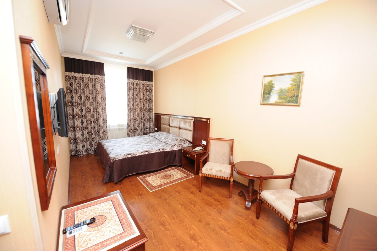 A hotel room with a bed, two chairs, a small table, a mirror, and a painting on the wall.