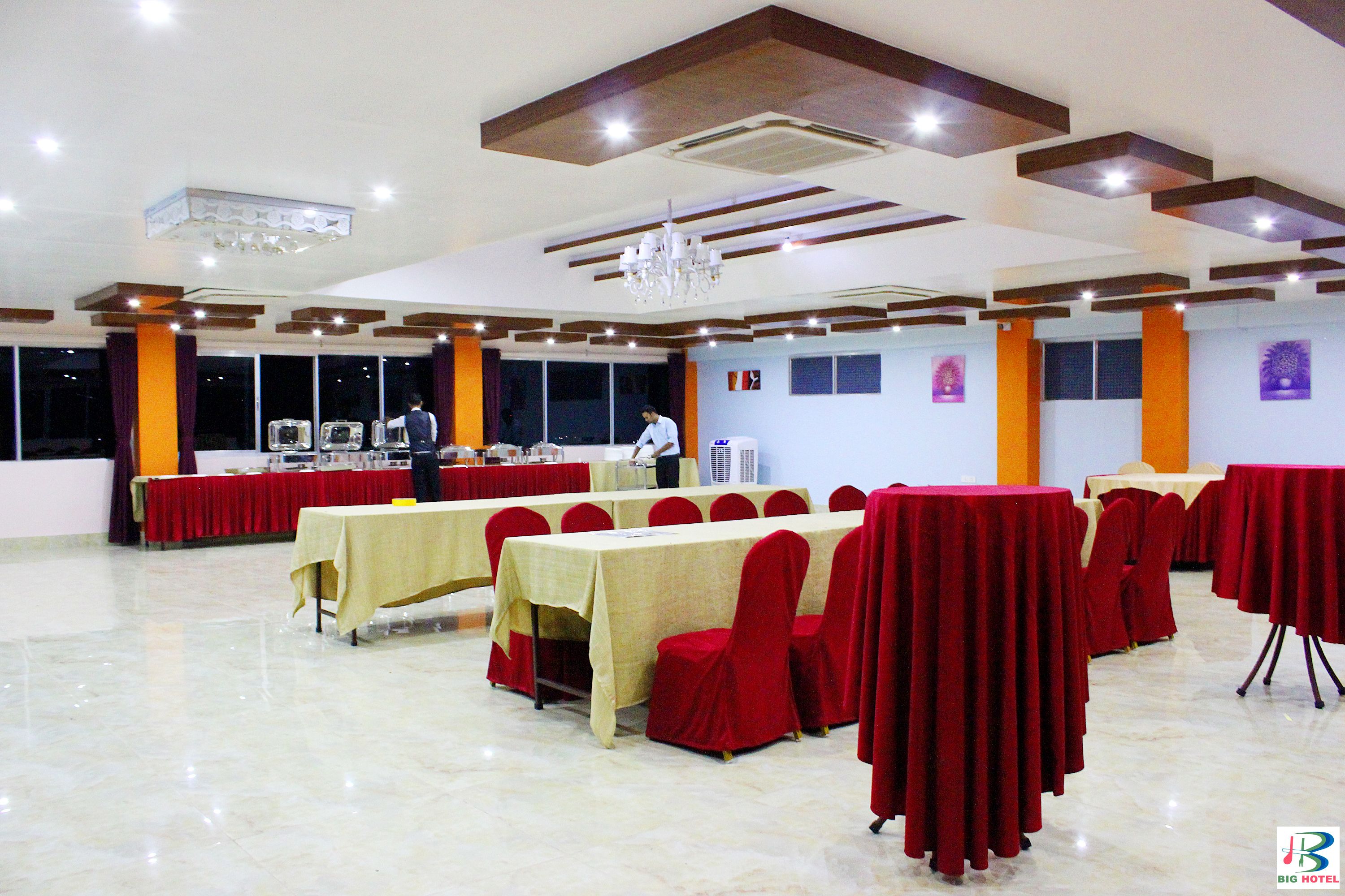 Un salón de banquetes con mesas dispuestas para eventos, una araña y una persona al fondo.