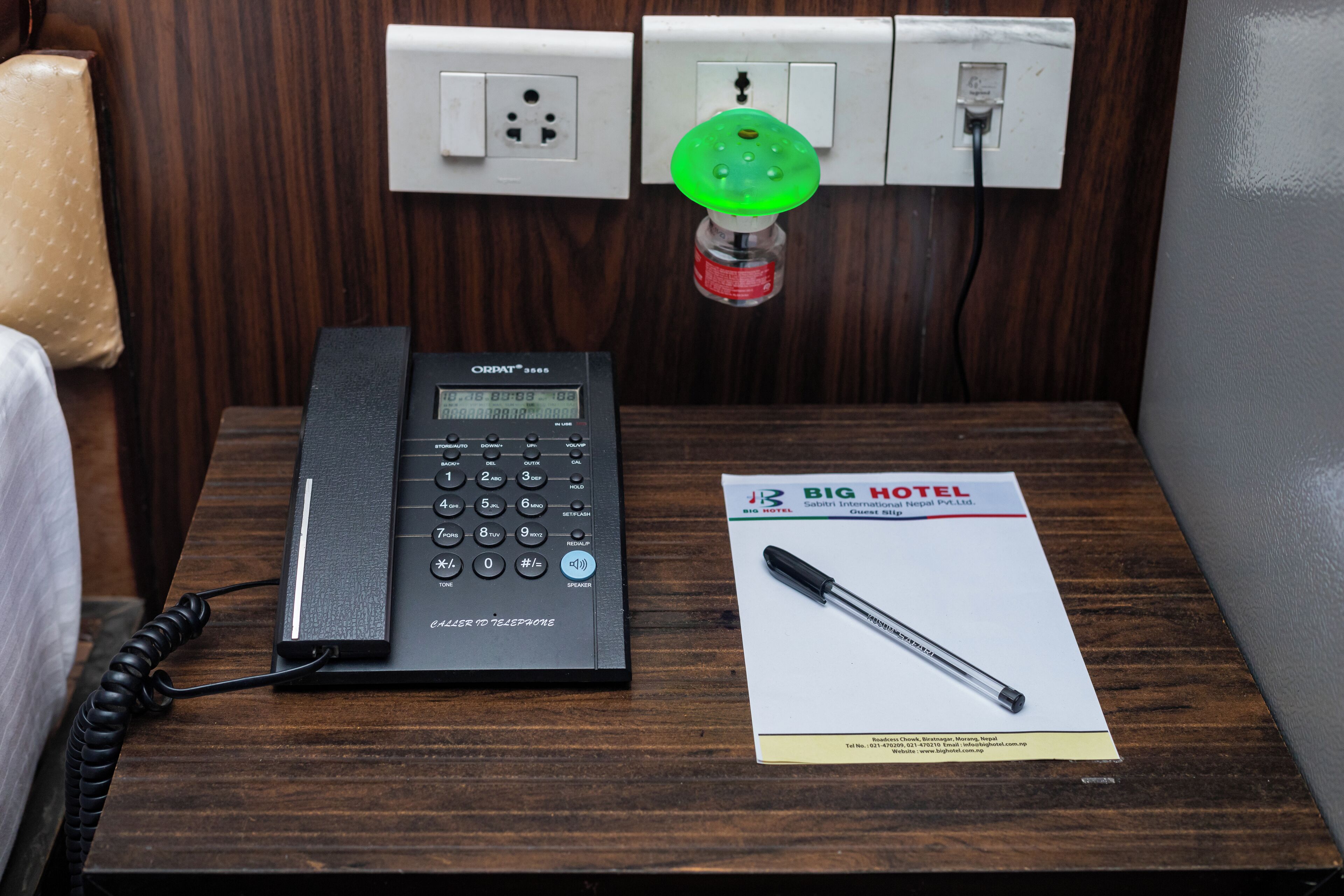 A hotel room with a telephone, a brochure, and a green light fixture on the wall.