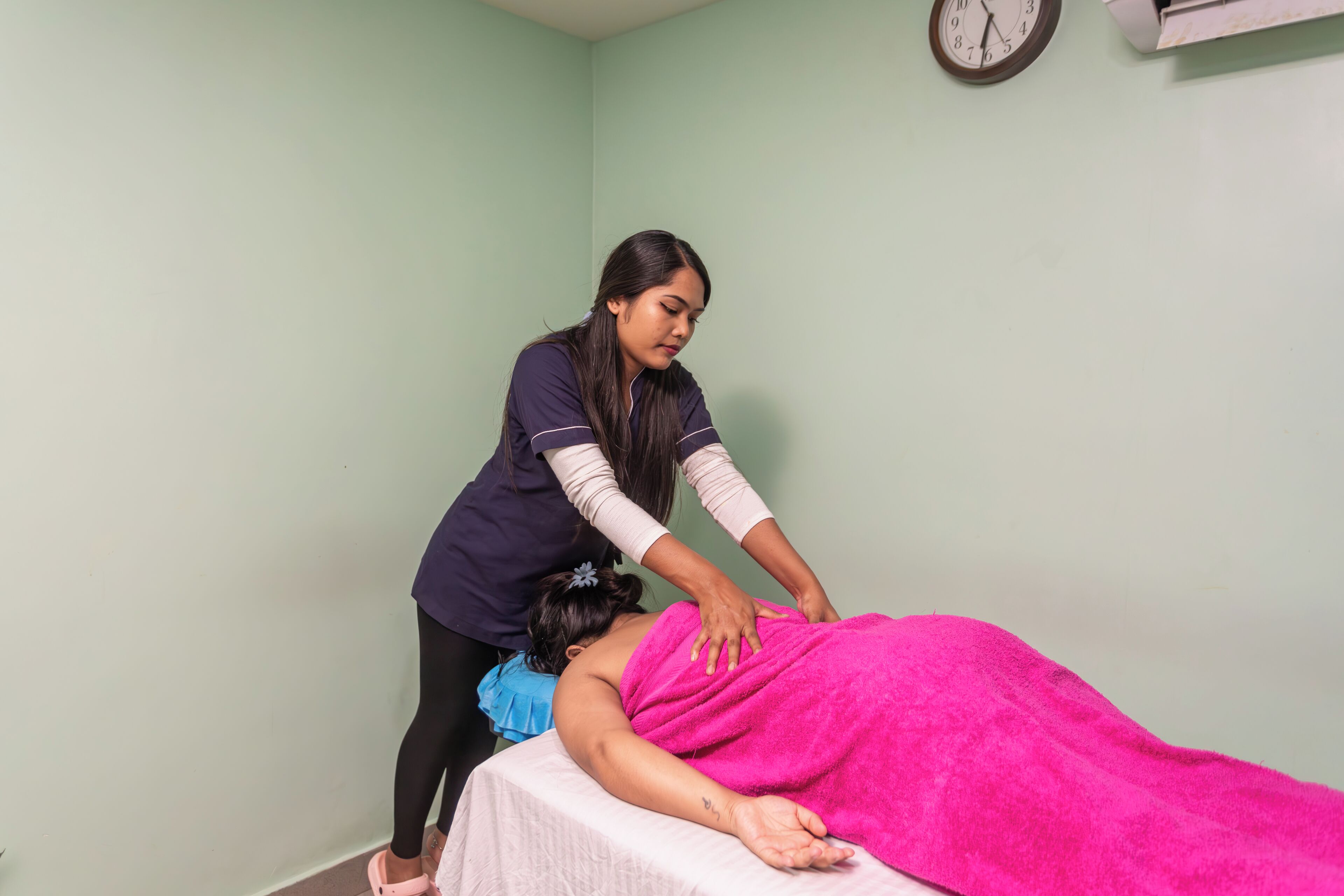 A massage therapy session in a room with a clock on the wall and a clock on the wall.