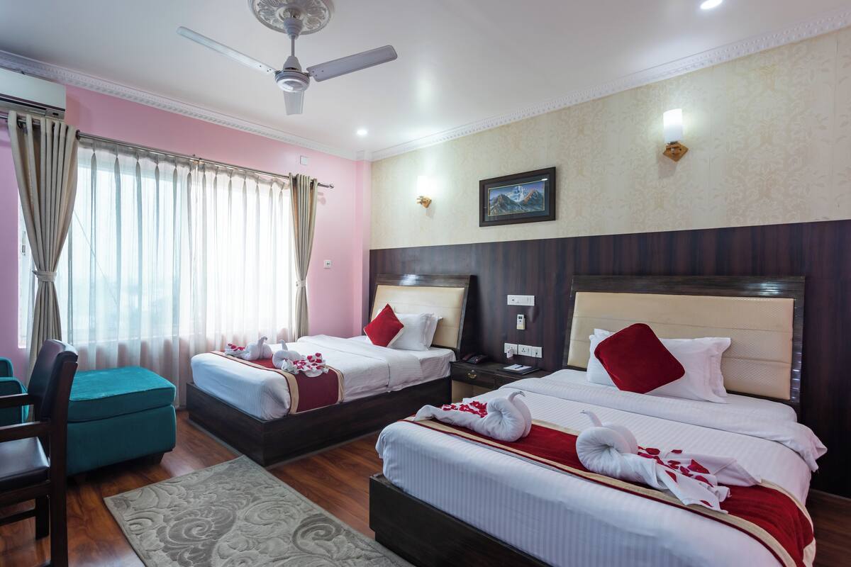 A hotel room with two beds, a desk, a chair, and a ceiling fan.