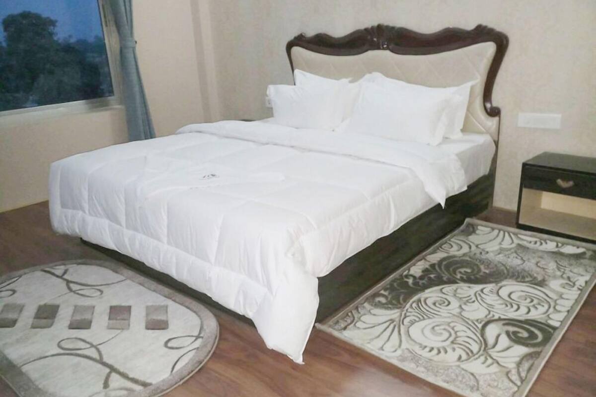 A neatly made bed with white linens, a wooden headboard, and a patterned rug on the floor.