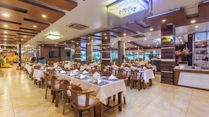 Un restaurant spacieux, doté de nombreuses tables et chaises, d’un comptoir et d’une grande fenêtre offrant une vue sur l’extérieur.