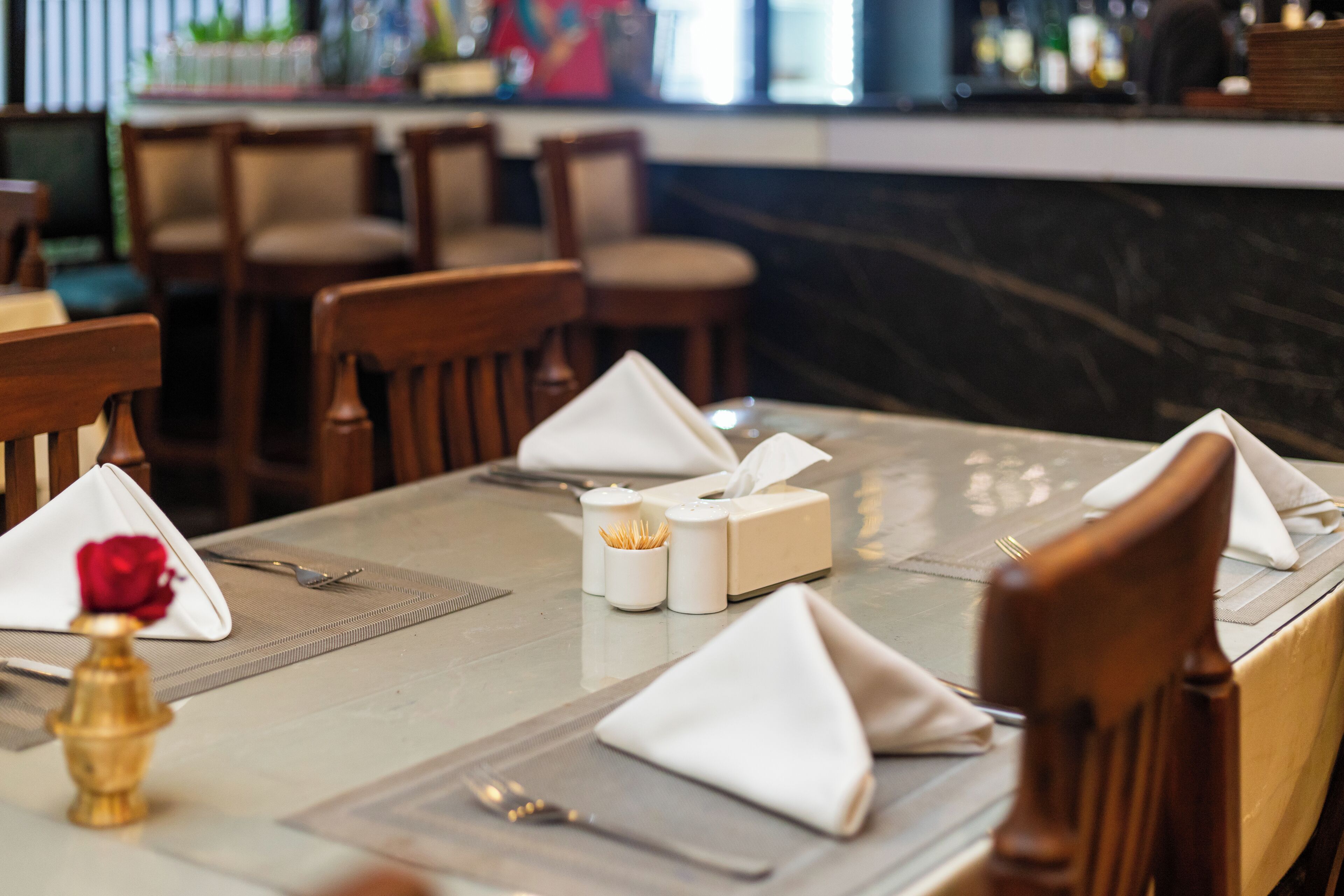 A dining table set with white napkins, a rose, salt and pepper shakers, and a small vase.