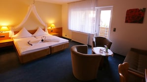 Une chambre d’hôtel avec un lit, une chaise, une petite table et une fenêtre avec des rideaux.