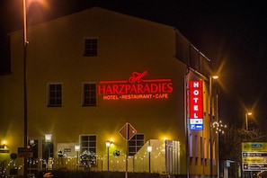 Un bâtiment sur lequel est apposée une grande enseigne indiquant « Harzparadies Hotel Restaurant Cafe » et une plus petite enseigne signalant un espace de stationnement.