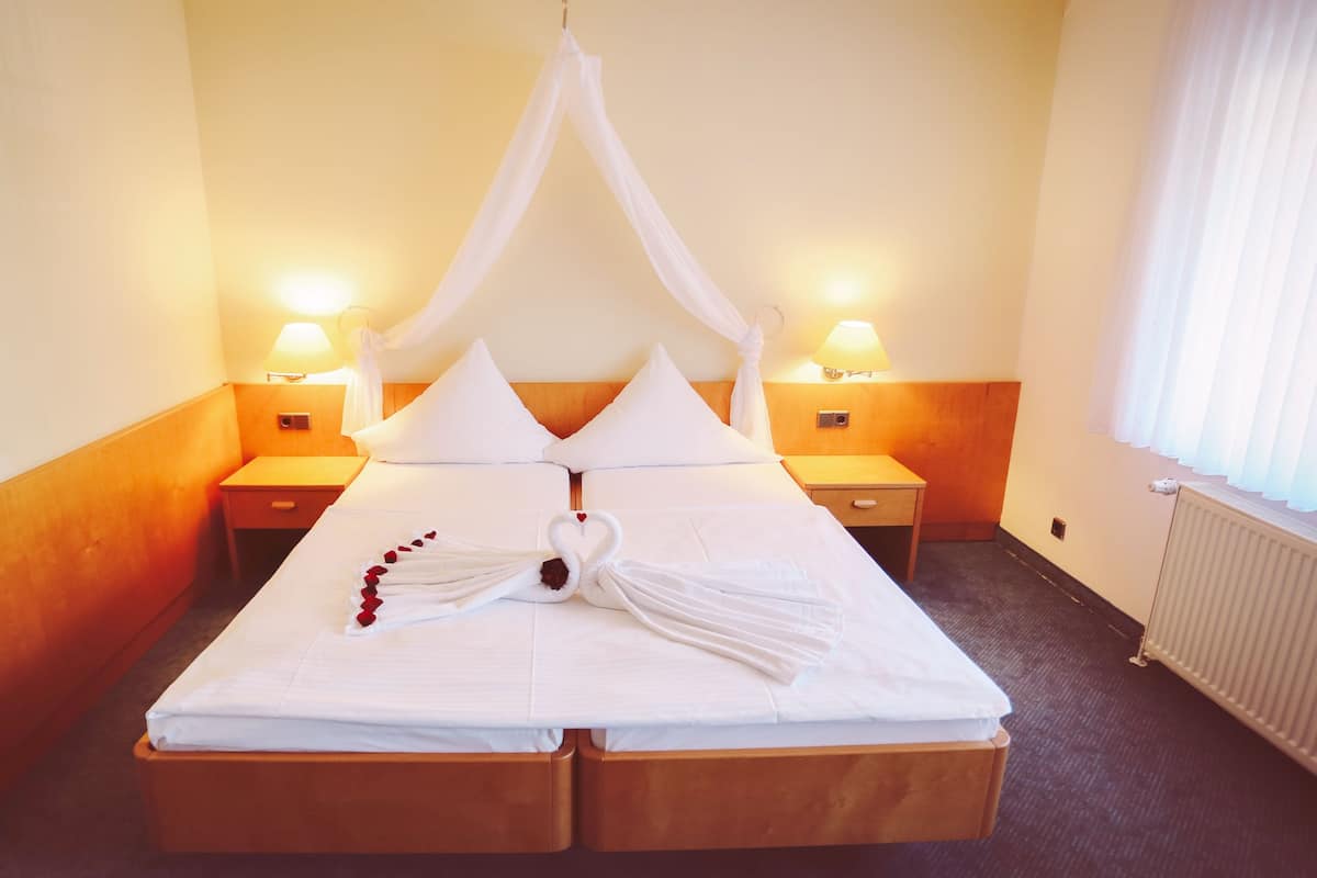 Une chambre d’hôtel avec un lit à baldaquin, deux lampes de chevet, une tête de lit en bois et un radiateur.
