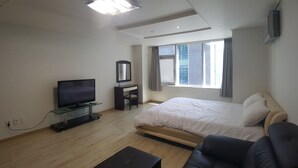 Moderni hotellihuone, jossa on suuri sänky, taulutelevisio, työpöytä ja ikkuna, jossa on verhot.