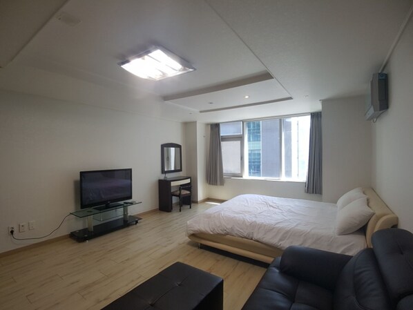 A modern hotel room with a large bed, a flat-screen TV, a desk, and a window with curtains.