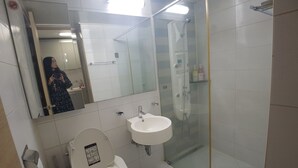 Moderni kylpyhuone, jossa on wc, pesuallas ja lasiseinällä varustettu suihku.