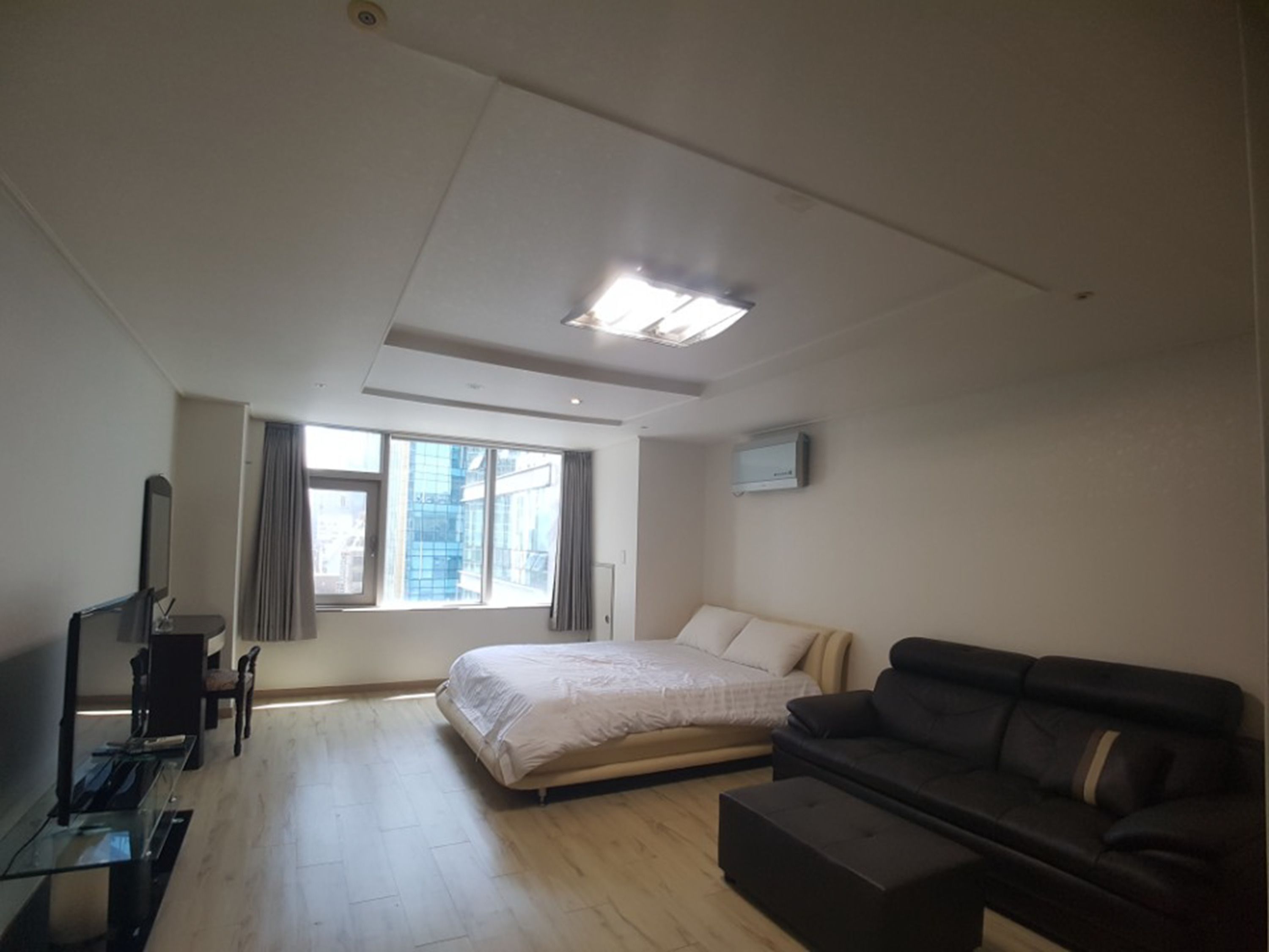 A modern hotel room with a bed, a sofa, a TV, and a desk.