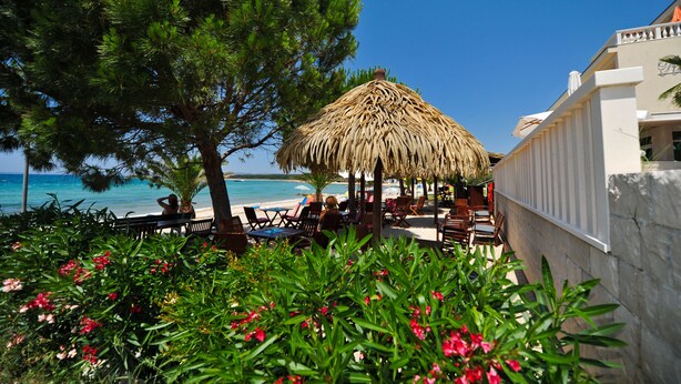 A beachside restaurant with outdoor seating, a thatched umbrella, and a view of the sea. - Villa Kastel (Povljana)