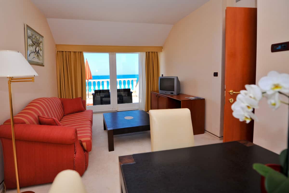 A hotel room with a sofa, a small table, a television, and a balcony with a view.