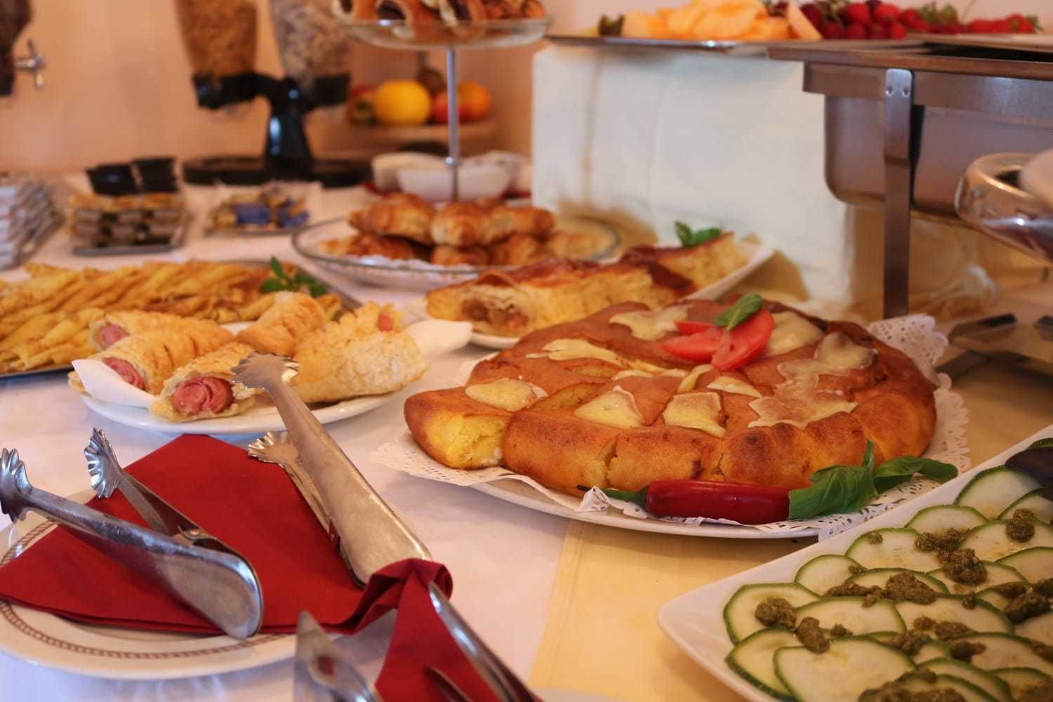 A buffet with various dishes including pastries, a fruit platter, and a vegetable dish.